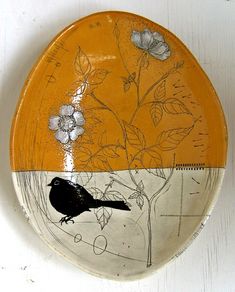 a yellow plate with a bird on it and flowers painted on the side, sitting on a white surface