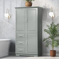 a white bath tub sitting next to a tall gray cabinet with drawers and plants on top