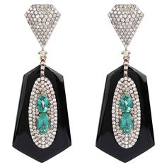 18.00 Carats Diamond, Emerald, and Black Onyx Drop Earrings in Art-Deco Style Feel unique with this scintillating and artistic set of earrings. The exquisite and artistic design with which this set of earrings is crafted, speaks a lot about it. This combination of black onyx, diamonds and emerald is what makes this pair of earrings a style statement. This art-deco style set of earrings is exceptional and a head-turner. The lower half of the earrings is crafted with an oval-shaped and one teardrop-shaped emerald placed opposite to each other. These pieces of emeralds are further surrounded by a cluster of diamonds in 3 consecutive halos making the emeralds stand out and look absolutely amplifying. These beautiful pieces of emerald are embellished over hexagon shaped tubes of black onyx exqu Luxury Black Art Deco Earrings, Luxury Black Diamond Earrings, Luxury Black Diamond Earrings For Evening, Luxury Diamond Gemstone Earrings For Party, Formal Black Diamond Earrings Fine Jewelry, Luxury Diamond Earrings For Evening With Polished Finish, Fine Jewelry Polished Finish Evening Earrings, Fine Jewelry Evening Earrings With Polished Finish, Exquisite Gemstone Earrings For Evening