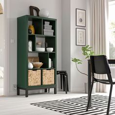 a green bookcase with wicker baskets on it in a white living room next to a black chair