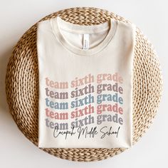 a white t - shirt with the words team middle school printed on it sitting next to a wicker basket