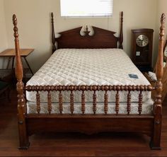 there is a bed with wooden posts and white sheets in the room, it has a clock on the wall