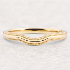 a yellow gold wedding band with beaded edges on a white marble surface, close up