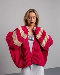 a woman is wearing a pink sweater and holding her hand on her shoulder while standing in front of a gray wall