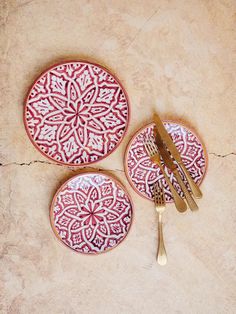 three red and white plates sitting on top of a table next to gold utensils