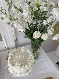 a white cake sitting on top of a table next to a vase filled with flowers