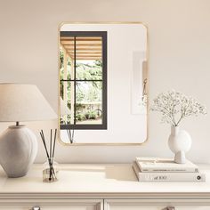 a white dresser topped with a mirror next to a lamp and vase filled with flowers