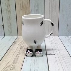 a white coffee mug with black and white cats on it's sides sitting on a wooden table