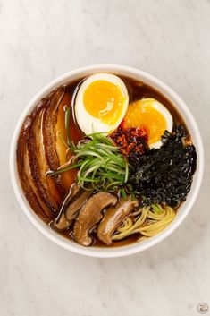 an overhead view of a bowl of ramen with eggs, mushrooms, and greens