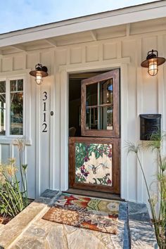 the front door of a white house with flowers and plants on it's side