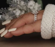 a woman's hand holding a diamond ring on top of her finger with flowers in the background