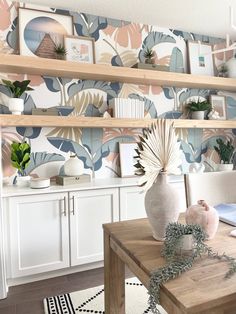 a dining room table with vases and plants on the shelf above it, in front of wallpapered shelves