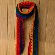 a multicolored crocheted scarf hanging on a wooden wall