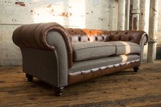 a brown and tan leather couch sitting on top of a wooden floor next to a brick wall