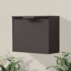 a black box mounted to the side of a white wall next to potted plants