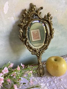 an apple sitting next to a mirror on top of a lace tablecloth with pink flowers in front of it