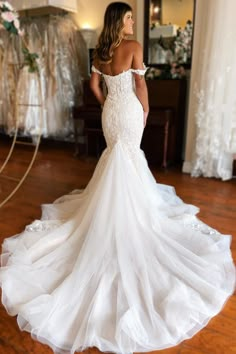 a woman in a white wedding dress standing on a wooden floor with her back to the camera