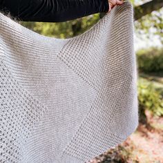 a woman holding up a white knitted shawl