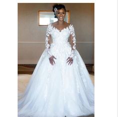 a woman wearing a white wedding dress with long sleeves and lace on the top, standing in front of a mirror