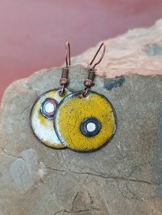 two yellow and black circles are hanging from brown hooks on a rock with pink water in the background