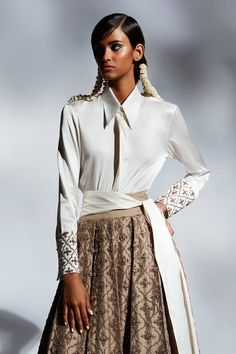 Ivory satin shirt with straight collar, Mughal motifs, contrast metallic cut dana and zari embroidered sleeve cuffs.
Components: 1
Pattern: Embroidered
Type Of Work: Cut Dana and Zari Work
Neckline: Straight Collar
Sleeve Type: Full Cuff Sleeves
Fabric: Satin
Color: Ivory
Other Details: 
Broad sleeve cuffs
Closure: Front concealed hook and eye
Note: The belt, lehenga and hair accessory worn by the model is not for sale
Occasion: Party,Cocktail - Aza Fashions White Silk Blouse For Semi-formal Occasions, Semi-formal White Silk Blouse, Elegant Cream Blouse For Festive Season, Formal Blouse With Embroidered Sleeves, Elegant Blouse With Embroidered Sleeves For Wedding, Formal Long Sleeve Blouse With Embroidered Cuffs, Elegant Wedding Blouse With Embroidered Sleeves, Elegant Semi-formal Festive Shirt, Elegant Fitted Tops With Embroidered Cuffs