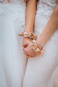 two brides holding hands with flowers on their wrist and wearing bracelets that are gold and white