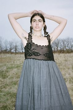 a woman standing in a field with her hands on her head and wearing a dress