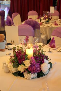 the centerpieces on this table are adorned with purple and white flowers, candles and napkins