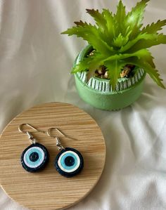 a pair of blue and black earrings sitting on top of a wooden tray next to a potted plant