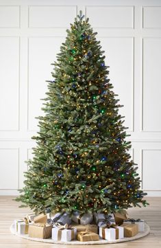 a christmas tree with presents under it on a wooden floor in front of a white wall