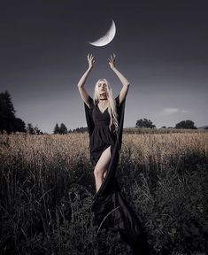 a woman in a black dress is holding a half moon above her head while standing in a field