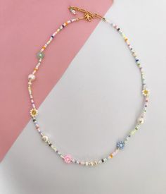 a multicolored beaded necklace on a pink and white background with a gold charm