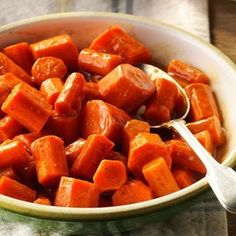 a white bowl filled with cooked carrots on top of a wooden table next to a spoon