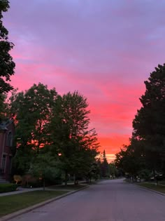 the sky is pink and purple as the sun goes down in this residential area with trees lining the street