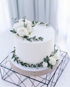 a white wedding cake decorated with flowers and greenery sits on a geometric wire stand