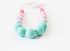 a close up of a beaded necklace on a white surface with a pink and blue cord