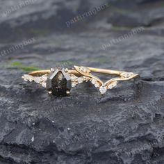 two gold rings with white diamonds on top of a black stone surface, one is shaped like a leaf and the other is shaped like an arrow