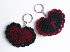 two crocheted heart shaped keychains on a white surface, one is black and the other is red