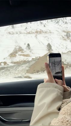 a person holding up a cell phone in the back seat of a car on a snowy day