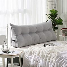 a bed with white sheets and pillows in a room next to a plant on a table