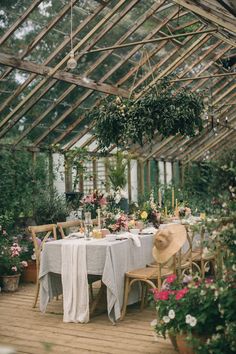 a table set up in a greenhouse with flowers and greenery