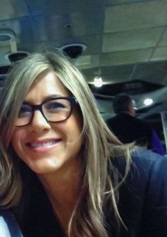 a woman wearing glasses is smiling for the camera while sitting in a car with other people behind her