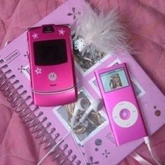 a pink cell phone sitting on top of a notebook next to an mp3 player and headphones