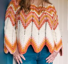 a woman standing in front of a door wearing a crocheted sweater and jeans