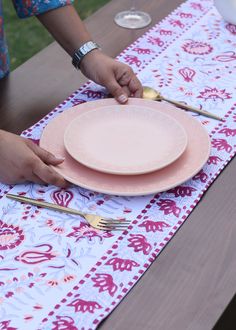 a person is setting a pink plate on a floral table cloth with goldware and silverware