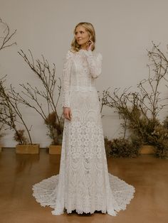 a woman in a white wedding dress standing next to some branches and flowers with her hand on her face