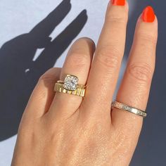 a woman's hand with two rings on it and an orange manicured nail polish