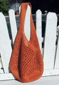 an orange crocheted purse sitting on top of a wooden bench next to a white fence