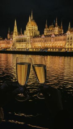 two glasses of wine sitting on top of a table next to a body of water