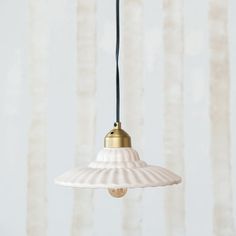 a white lamp hanging from a ceiling in front of a striped wallpapered background